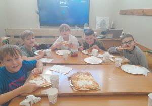 Chłopcy jedzą przygotowaną pizzę.