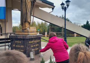 Uczennica składa znicz pod pomnikiem Jana Pawła II